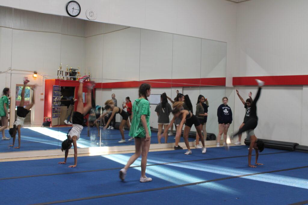 The cheer team practices tumbling in a snaking pattern.