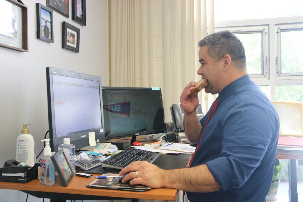 Principal Greg Louie steals a big bite of his patented peanut butter and jelly sandwich, while checking his email.