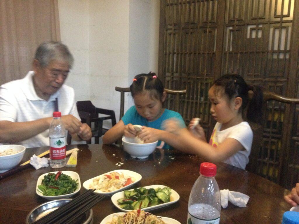 With their grandpa, sophomore Kathy Wang and her sister, with their matching braided hairstyles, tear up bread to make paomo, a popular Chinese soup.