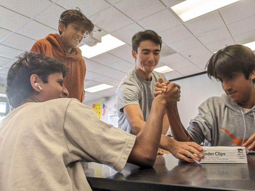 Naveed Kasnavi holds binder clips to mark 2 inches above table as sophomores Samvrith Bandi (left) and Akash Gupta (right) arm wrestle during a club meeting on Oct. 19. 
