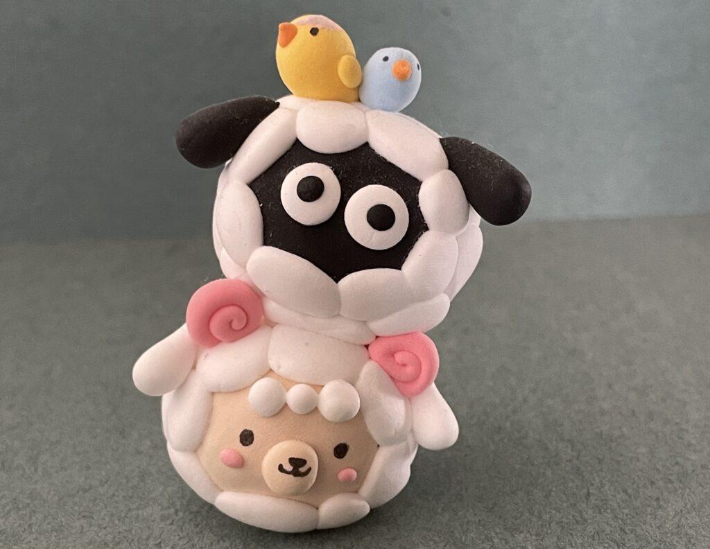 Dong finishes a clay stack of animals, with two sheep stacked on top of each other and one yellow and one blue bird on top.