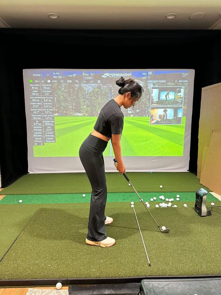 Junior Sarah Lim prepares to hit a ball in front of her, towards a projector-screen golf simulator.