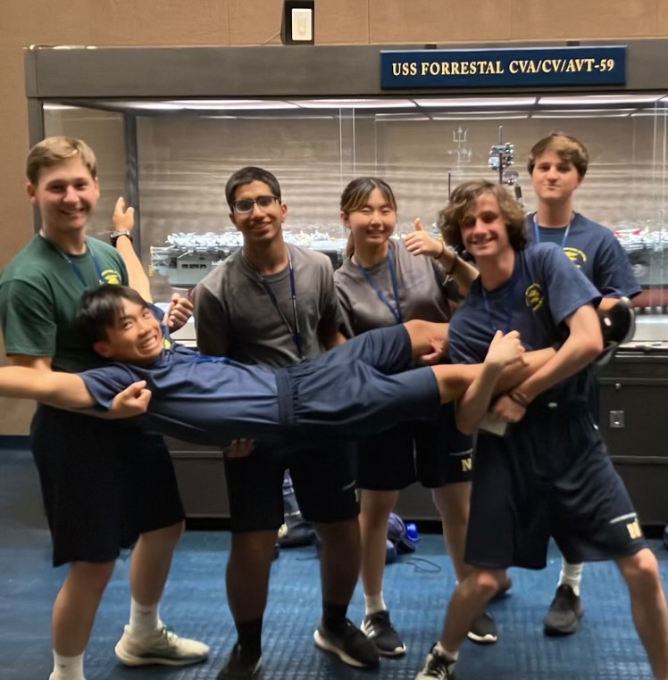 Seniors pose in front of a model ship at the United States Naval Academy.