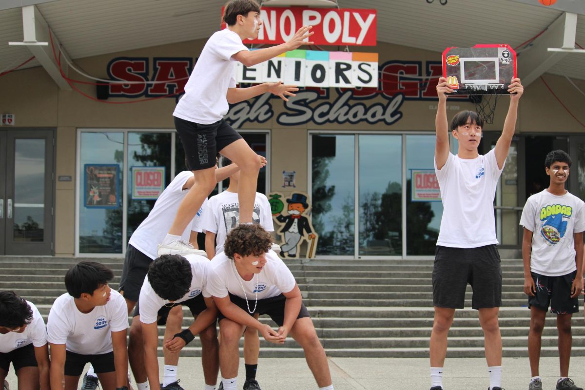 Benjamin Bolger prepares to dunk a basketball in a hoop, held by sophomore Ian Hu.