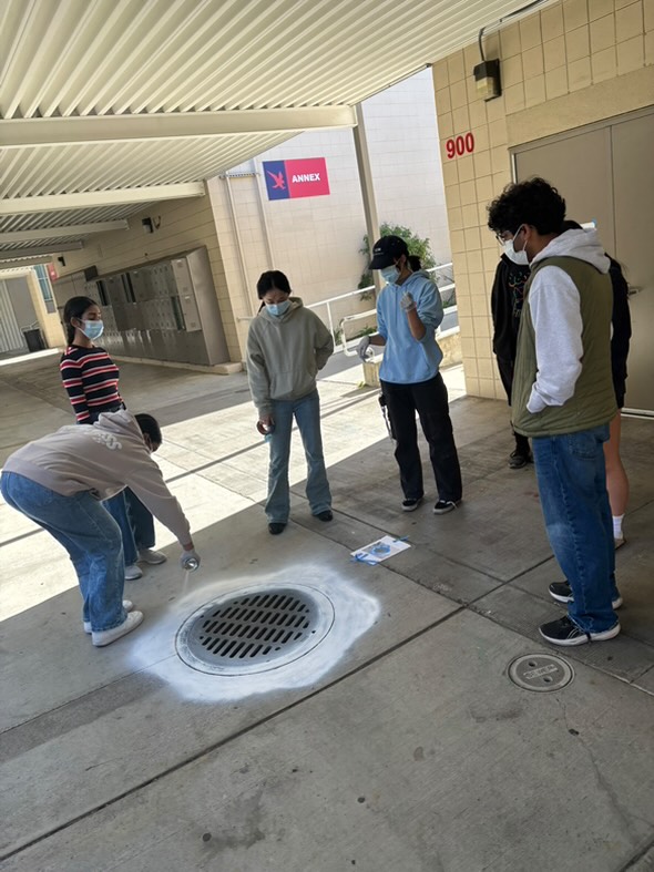 Students collaborate to paint the drain near the Media Arts Program Annex.