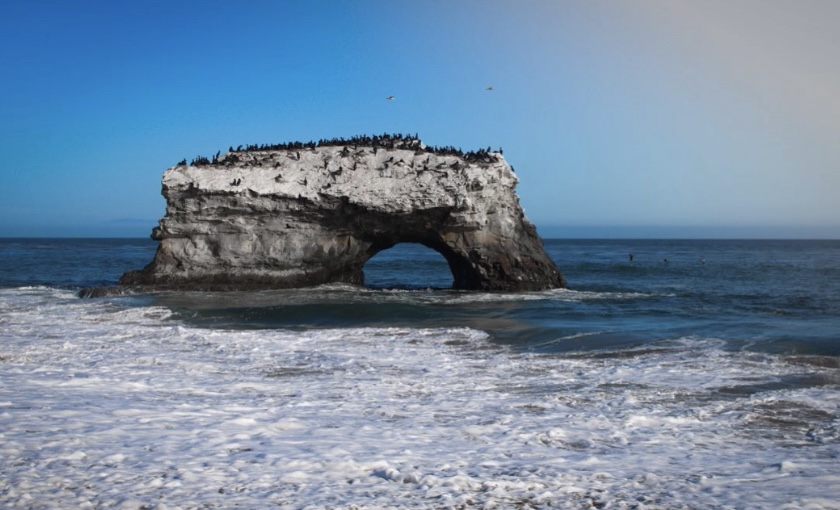 The rocky arch stands against a deep blue ocean and light blue sky.