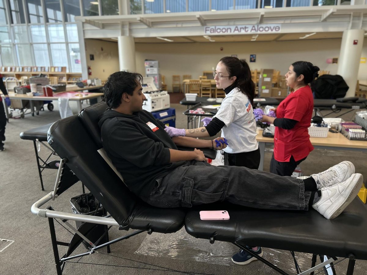 A Red Cross worker helps senior Arjun Bawa prepare for a blood donation.
