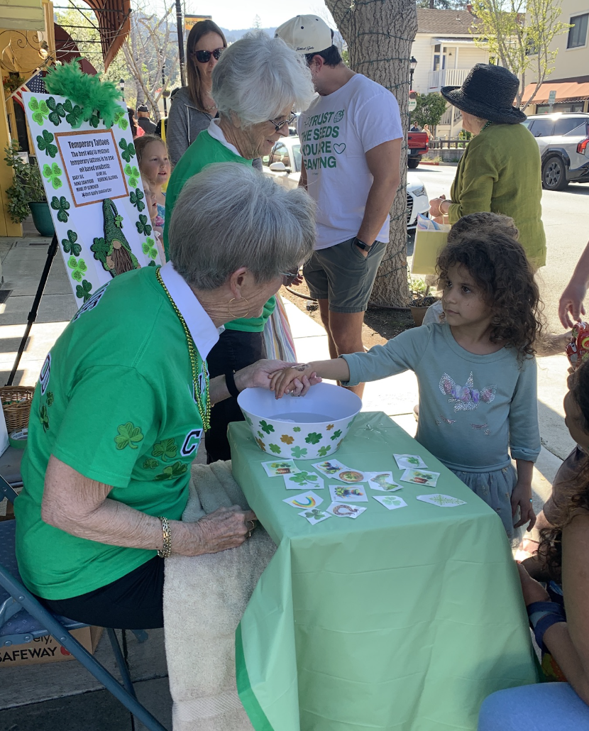 A group applies Saint Patrick’s Day themed tattoos like clovers and gold pots to children.